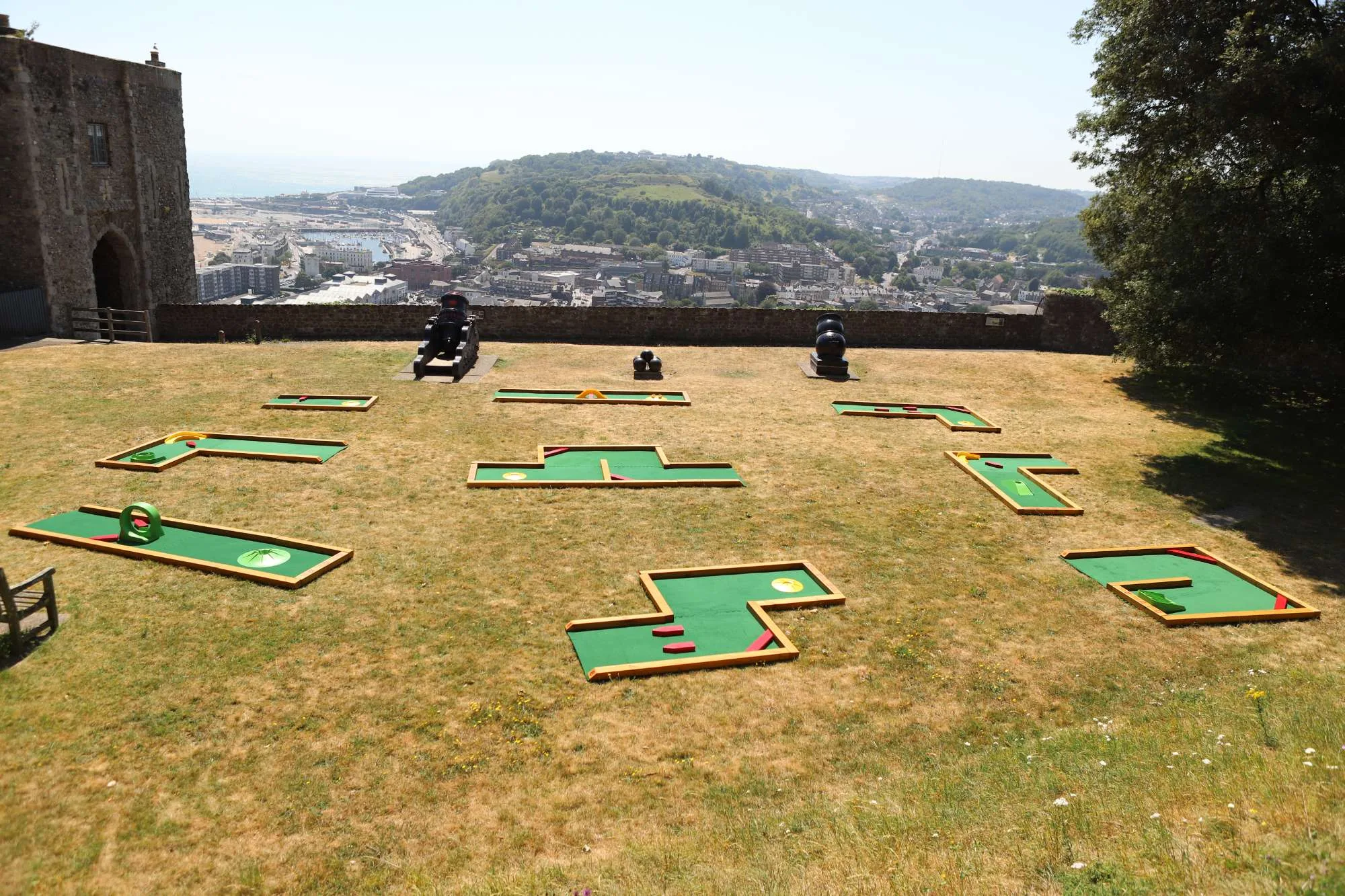 Six Putterfingers semi-permanent mini golf courses laid out on the sun-baked grass of Dover Castle's hilltop grounds, with historic cannons and the town and harbour visible below
